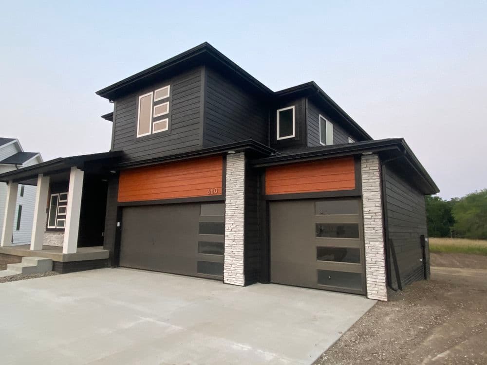 Modern black house with stone accents and double garage doors on a concrete driveway.