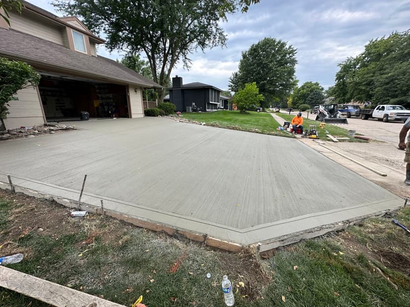 Freshly poured concrete driveway outside a residential home, with workers completing the project.